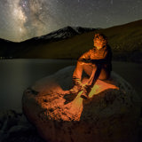 A man sits on a rock under the stars.